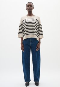 Maglione a righe beige con strisce orizzontali nere, vestibilità ampia e scollatura a barca; abbinato a jeans a vita alta blu scuro a gamba larga.