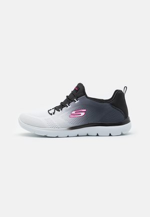 Skechers sportieve schoen in wit, grijs en zwart. Heeft een gestructureerde bovenkant, zwarte veters en een roze logo accent aan de zijkant.