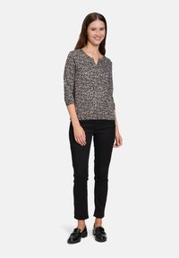 Gemusterte Bluse in Schwarz, Weiß und Beige mit V-Ausschnitt und Dreiviertelärmeln, kombiniert mit schwarzen Slim-Fit-Hosen und schwarzen Slippern.