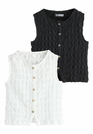 To ærmeløse cardigans med struktureret strik og knapper foran, en i hvid og en i sort, lagt fladt uden baggrund.