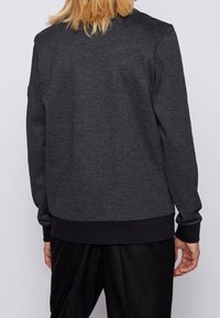 Mörkgrå sweatshirt med ett texturerat stickmönster, ribbade ärmar och nederkant. Har en klassisk design med rundad hals och detaljer på baksidan.