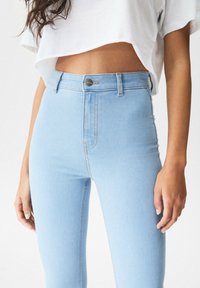 Jeans de mezclilla de tiro alto en un tono azul claro, con una textura suave, realzados por un botón metálico y costuras de contraste a lo largo de las costuras.