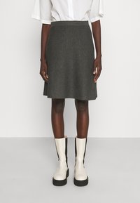 Falda de lana gris con un diseño acampanado, que presenta líneas de costura verticales. Combinada con botas altas hasta la rodilla en tonos beige y negro.