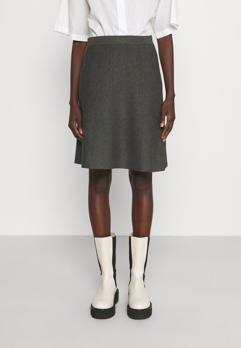 Falda de lana gris con un diseño acampanado, que presenta líneas de costura verticales. Combinada con botas altas hasta la rodilla en tonos beige y negro.