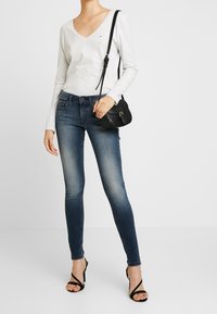 Světle šedý dlouhý rukáv V-výstřih top, který je spárován s tmavě modrými skinny džíny. Černá kabelka přes rameno s uzávěrem. Černé sandály na vysokém podpatku se řemínky.