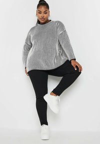 Maglione oversize a righe bianche e nere con spalle scese, abbinato a leggings neri e sneakers bianche, che mettono in evidenza un taglio rilassato.