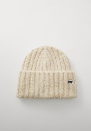 Cream-colored ribbed knit beanie made of soft wool, featuring a small silver and black logo detail on the front.