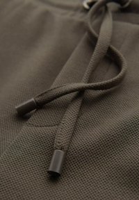 Mörkgrön texturerad tyg med snörning, som har metalliska aglets och ett nätliknande mönster. Närbild som betonar materialdetaljer.