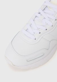 White sneaker featuring a smooth leather upper, round toe, and textured accents. Laces are flat, with a stitched design and visible air cushioning.