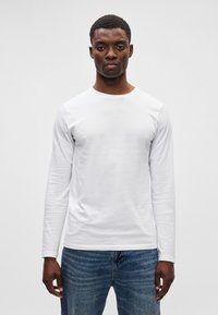 Hvit langermet T-skjorte i en tettsittende design med rund hals, laget av glatt stoff, sammen med blå denimjeans.