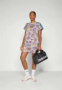 Robe courte grise avec des imprimés graphiques colorés, accents d'épaule bleus, associée à un sac noir portant la mention "adidog" et des baskets beiges.