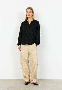 Mustasta, pitkähihainen pusero, jossa on V-aukko ja nappilista, koristeltu teksturoiduilla kukkakuviolla. Yhdistetty beigen värisiin leveälahkeisiin housuihin.