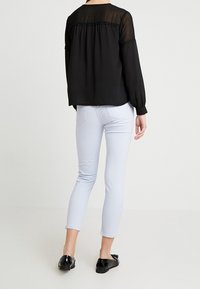 Schwarzes Langarmoberteil mit strukturiertem Mesh-Einsatz, kombiniert mit hellblauen engen Jeans und schwarzen glänzenden Loafers.