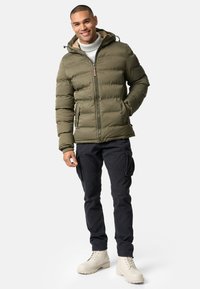 Oliven grønt puffer-jakke med hætte, quiltet design, frontlynlås og sidelommer. Båret med sorte cargo-bukser og beige støvler.