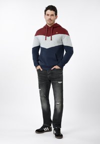 Φούτερ με κουκούλα σε συνδυασμό χρωμάτων βουργουνδίας, γκρι και ναυτικού μπλε. Συνδυασμένο με μαύρο τζιν με σκισίματα και μαύρα αθλητικά παπούτσια με λευκές ρίγες.