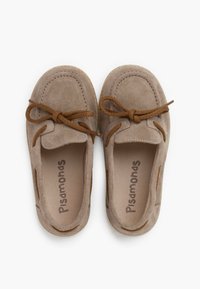 Zapatos de ante beige con una textura suave, punta redondeada y cordones decorativos marrones. Incluyen detalles recortados en los laterales y un logo en el interior.