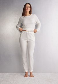 Witte lange mouwen top en bijpassende broek in geribbeld materiaal, met een ronde hals en een taille met trekkoord. Zachte, lichte textuur.