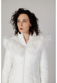 Veste blanche matelassée avec un col en fausse fourrure. Texture lisse, fermeture éclair et couture diagonale. Comprend des poches latérales.