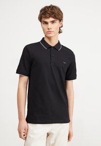 Black polo shirt made of cotton with a classic collar, two button placket, and white piping on the collar and sleeves. Small logo on chest.