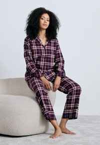 Βουργουνδί ανψόδι σετ πιτζάμων από μαλακό ύφασμα, με κουμπωτό γιακά και μακριά μανίκια, συνοδευόμενο από παντελόνια ίσιας γραμμής και μπλέ επισημάνσεις.