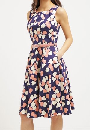 Blaues Kleid mit pink- und cremefarbenem Herzmuster, ärmelloses Design, taillierter Schnitt und knielanger Rock mit Taschen. Glatte Stoffstruktur.