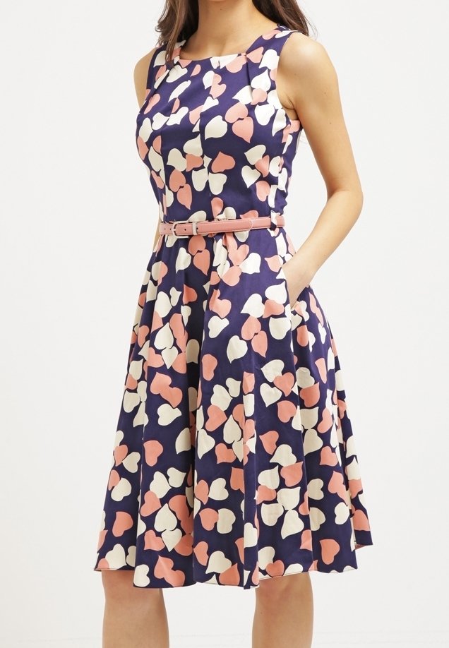 Blaues Kleid mit pink- und cremefarbenem Herzmuster, ärmelloses Design, taillierter Schnitt und knielanger Rock mit Taschen. Glatte Stoffstruktur.