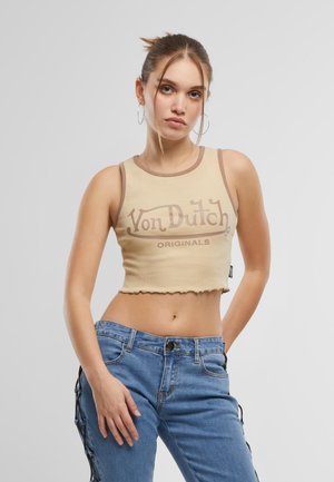 Bézs crop top barna szegéllyel, rajta barna színben "Von Dutch Originals" felirattal. Kék farmerral párosítva, oldalsó díszítésekkel és laza szabással.