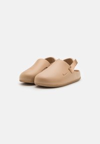 Zuecos de Nike en beige claro, fabricados en goma suave, con una correa trasera para mayor soporte, suela texturizada para un buen agarre y diseño minimalista.