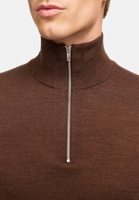 Maglione marrone con zip e colletto alto. Tessuto a coste testurizzato, con una zip argentata al collo. Vista ravvicinata del colletto.