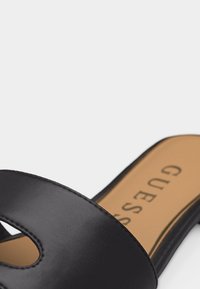 Μαύρο δερμάτινο σανδάλι με σαγιονάρα με ταμπά εσωτερική σόλα με το λογότυπο "GUESS", που διαθέτει λεπτομέρεια κοψίματος στο πάνω λουράκι.