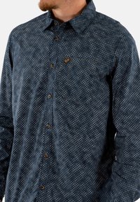 Donkerblauw overhemd met lange mouwen en een geometrisch patroon. Voorzien van een button-down kraag, een zak aan de voorkant en bruine knopen.