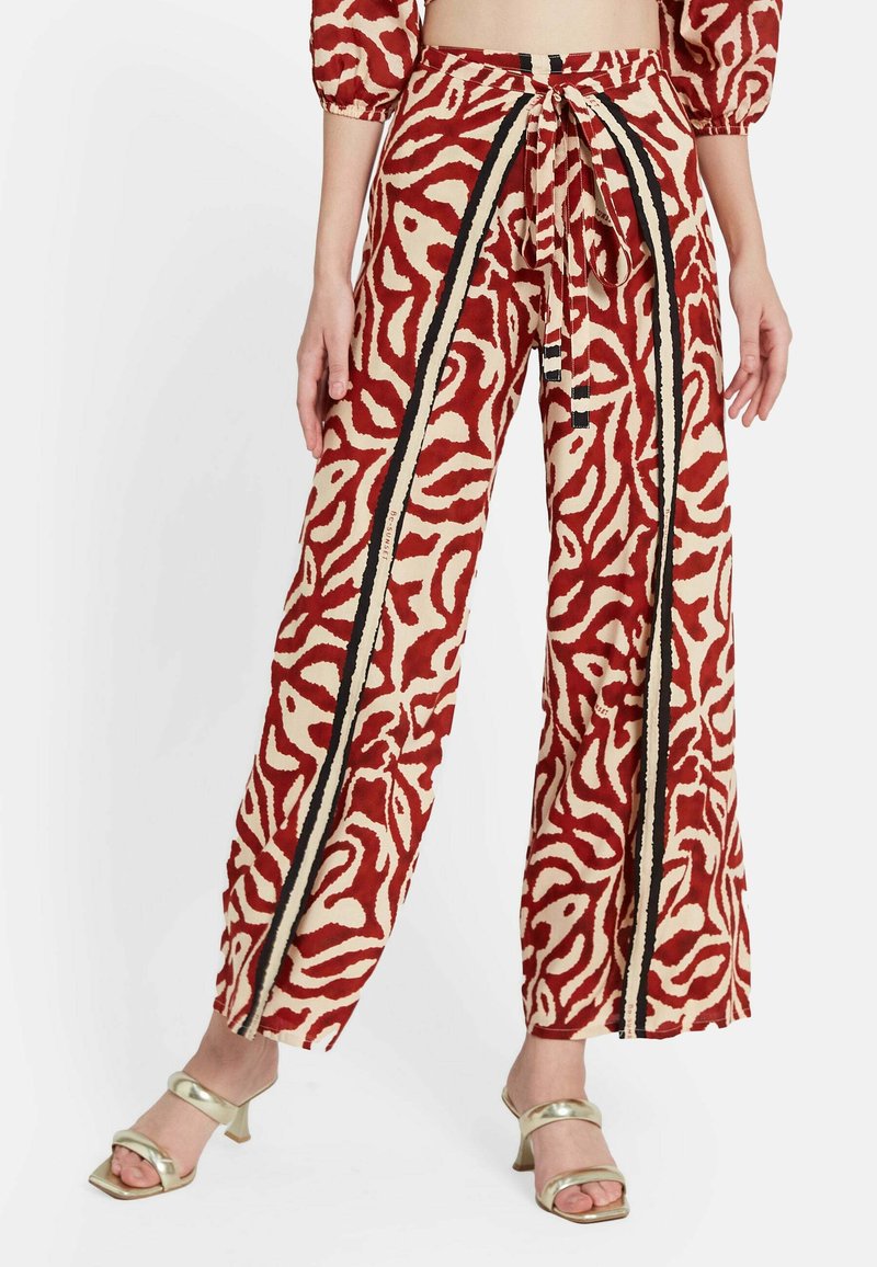 Pantalones de pierna ancha en beige con un patrón abstracto en rojo y crema. Tienen una cintura con cordón y rayas negras a los lados.