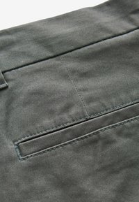 Tessuto grigio con una texture liscia, caratterizzato da una piccola tasca rettangolare e dettagli di cucitura blu a contrasto.