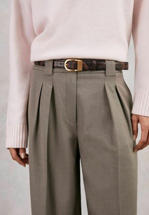 Smeđi pojas s uzorkom i zlatnom kopčom nošen preko sivih nabranih hlača, u kombinaciji s džemperom svijetlo ružičaste boje sa rebrastim manžetama.