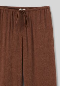 Pantalons de pyjama marron texturés avec une taille élastique, un lien de serrage et une coupe droite. Le tissu présente un motif à rayures subtil.
