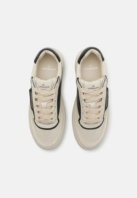 Baskets en cuir beige avec des accents noirs, bout rond, design à lacets, détails perforés sur la boîte à orteils et logo sur la languette.