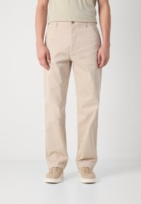Beige bomullsbukser med rett snitt, lett stoff og knappelukking foran. Kombinasjonen med beige sneakers fullfører stilen.
