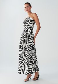 Axelbandslös svartvit klänning med zebramönster, figurnära liv och flödande kjol. Har volangdetaljer vid midjan och en mjuk textur.