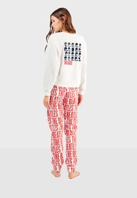 Sudadera blanca de cuello redondo con un gráfico cuadrado de rostros y el texto "THE BEATLES" en la parte posterior; pantalones rojos con un patrón que repite el texto "THE BEATLES".
