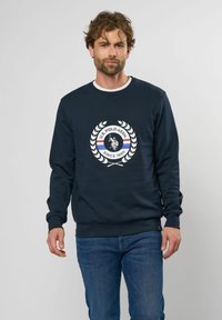 Marineblaues Sweatshirt mit rundem Halsausschnitt, ausgestattet mit einem zentralen runden Logo, das einen Polospieler und ein Lorbeer-Design zeigt. Ribbed Bündchen und Saum.