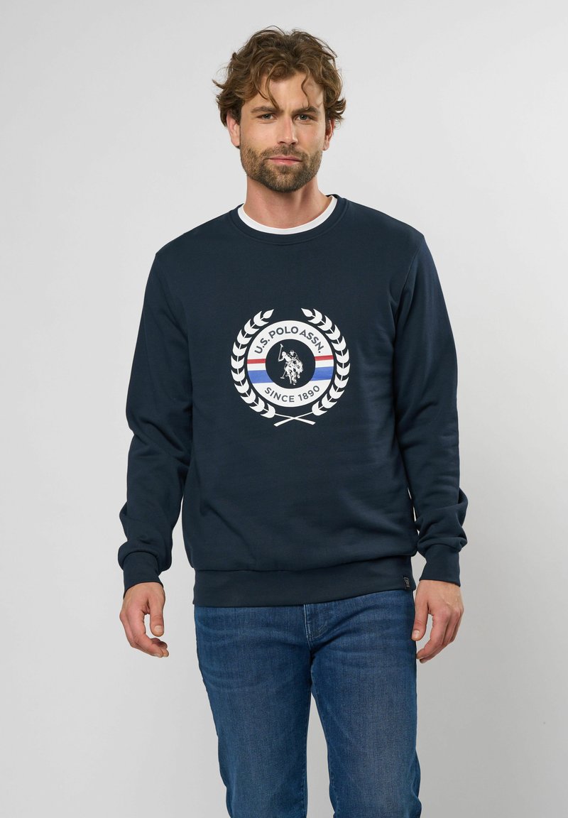 Marineblaues Sweatshirt mit rundem Halsausschnitt, ausgestattet mit einem zentralen runden Logo, das einen Polospieler und ein Lorbeer-Design zeigt. Ribbed Bündchen und Saum.