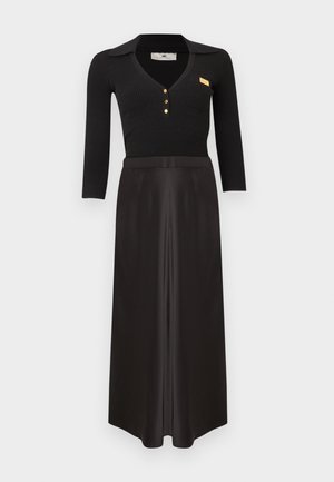 Top negru cu mâneci lungi, cu dungi și guler, cu nasturi aurii, asortat cu o fustă maxi neagră din satin cu talie înaltă, pe fundal alb.