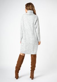 Hellgraues, gestricktes Turtleneck-Kleid mit ribbeliger Textur, langen Ärmeln und midi-langer Länge, kombiniert mit braunen, suedelangen Stiefeln.
