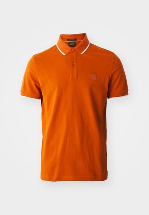 Polo shirt orange en coton, avec une patte de boutonnage à deux boutons, des accents blancs au col et aux manches, et un patch de marque.