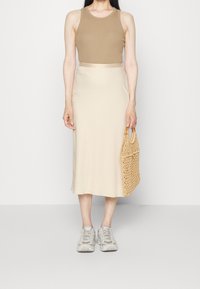 Top in cotone marrone chiaro, gonna midi beige e sneakers grigie chiare. Borsa in tessuto beige intrecciato con manici in legno. Design semplice.