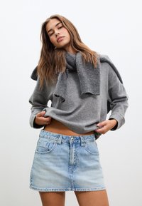 Grå stickad tröja med uppvikta ärmar, lager ovanpå en ljusblå denim minikjol med fransad nederkant och två framfickor.