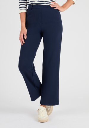 Navyblauwe wijde broek van een gladde stof, met een middelhoge taille en voorzakken, gecombineerd met crèmekleurige sneakers.