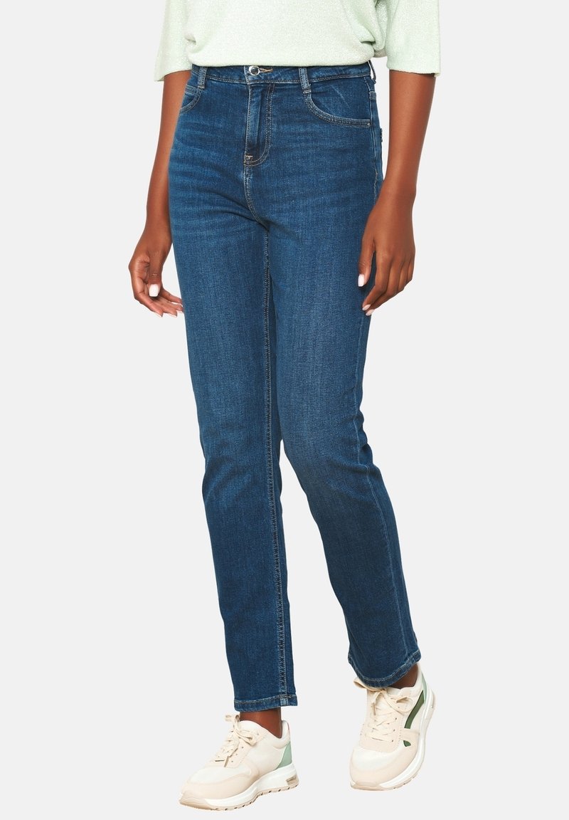 Mörkblå denimjeans med rak passform, hög midja och klassisk femfickdesign. Bärs med ljusa sneakers.