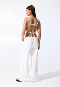 Bílé halter top bez zad, s tenkými ramínky, upevněný pomocí tkaniček. V kombinaci s širokými bílými kalhotami, které mají dvě zadní kapsy.