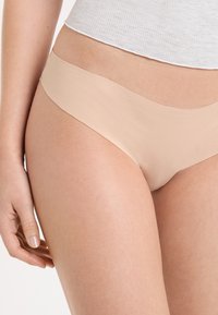 Culotte beige avec une ceinture élastique lisse et un tissu doux, présentant un design minimaliste sans coutures visibles.